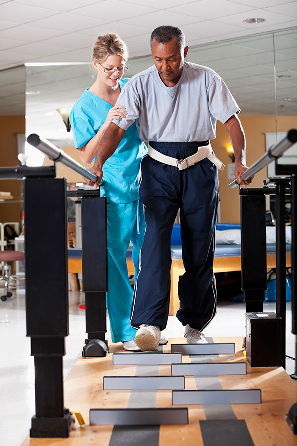 Physical therapist (30s) helping patient (60s) through gait training.