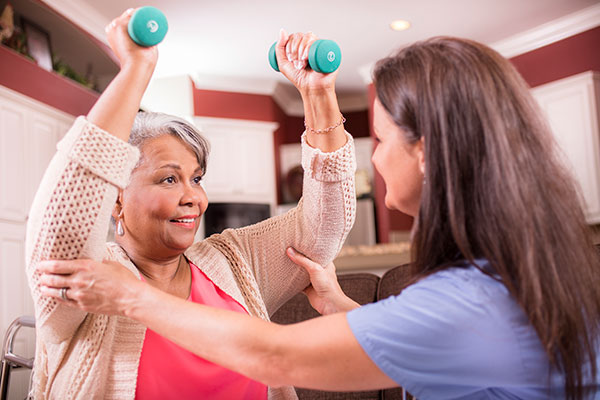 aring, Latin descent home healthcare nurse conducts physical therapy exercises with African descent senior adult patient at home, assisted living, or nursing home setting.